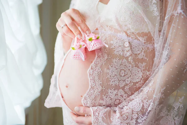 Femme enceinte tenant des chaussures de bébé roses sur son ventre — Photo