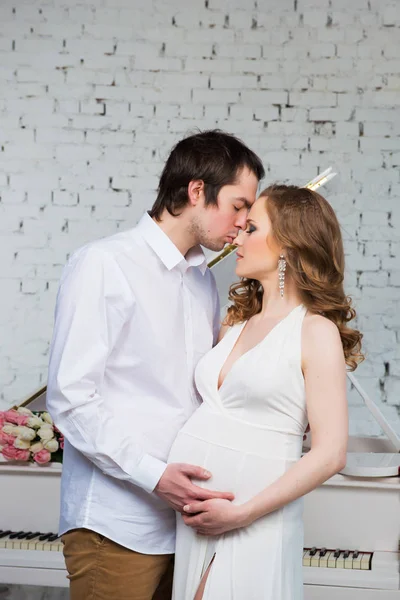 Prachtige paar, zwangere jonge vrouw en man knuffelen met liefde, op piano achtergrond. — Stockfoto