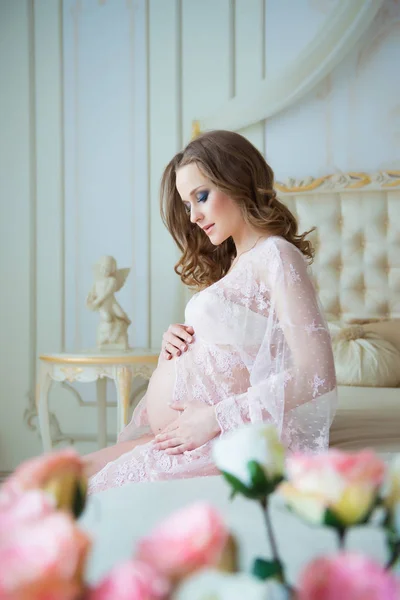 Gravidez, descanso, pessoas e conceito de expectativa - mulher grávida feliz sentada na cama e tocando sua barriga em casa. — Fotografia de Stock