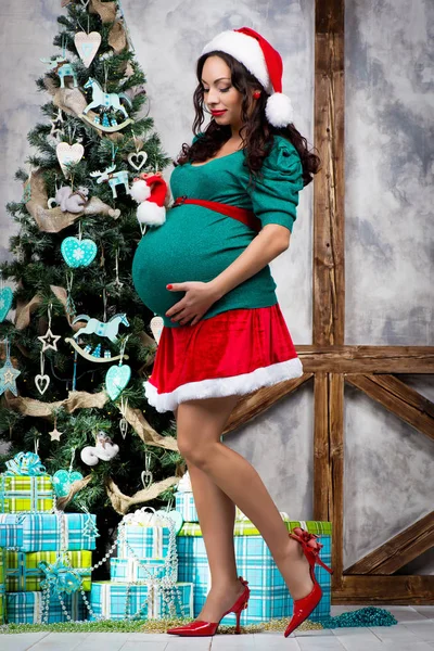 Беременная девушка в пинап-костюме рядом с елкой — стоковое фото