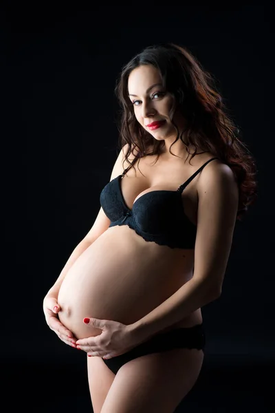 美丽的怀孕女人黑色内衣，在黑色背景上的工作室的肖像 — 图库照片