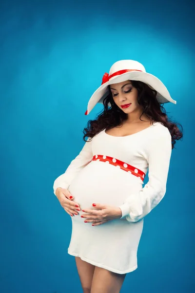 Hermosa joven embarazada en un vestido blanco sobre un fondo azul — Foto de Stock