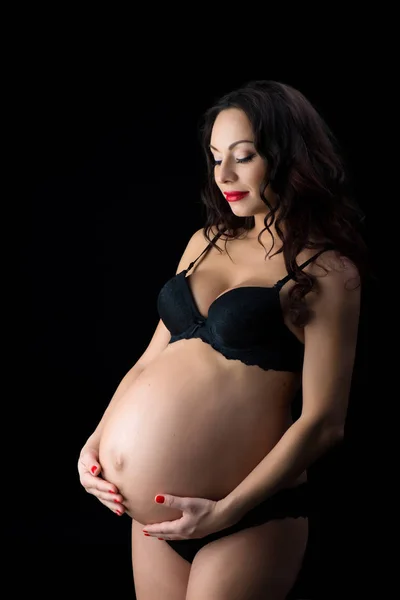 Portret van een mooie zwangere vrouw in zwarte lingerie, studio op een zwarte achtergrond — Stockfoto