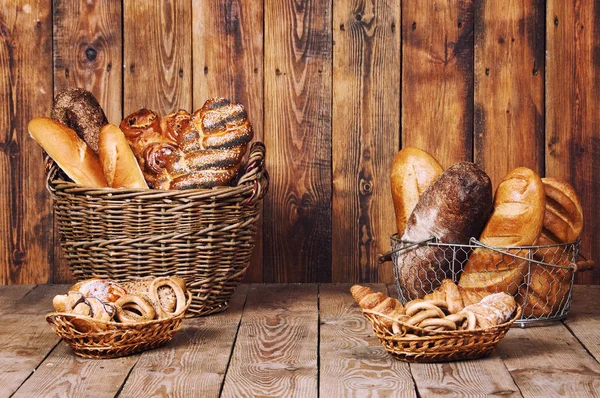 Verschiedenes Brot mit Ohren im Korb auf Holzgrund — Stockfoto