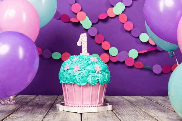 Kue ulang tahun pertama dengan unit pada latar belakang ungu dengan bola dan karangan bunga kertas . — Stok Foto