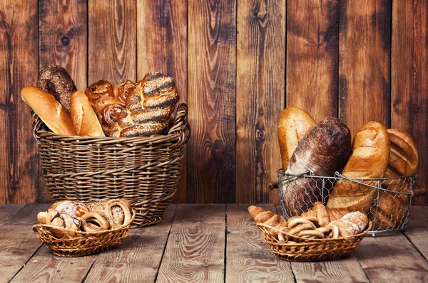 Verschiedenes Brot mit Ohren im Korb auf Holzgrund — Stockfoto