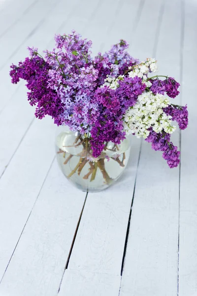 En bukett med friske syrinblomster i en glassvase på et tregulv . – stockfoto