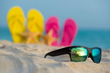 Sarı ve pembe sandalet gözlükle deniz arka planı kum stand