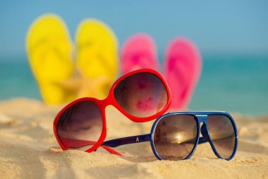 Sarı ve pembe sandalet gözlükle deniz arka planı kum stand
