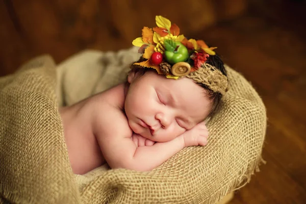 Een schattige baby in een krans van bessen ligt in een mandje. — Stockfoto