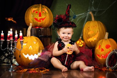 Küçük cadı şeker kabaklar ve mumlar arasında el ile gülüyor.