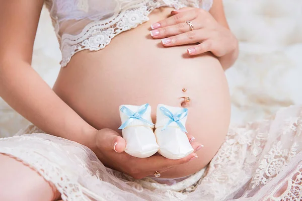 Baby laarsjes op de achtergrond van de buik. Wachten voor de baby — Stockfoto