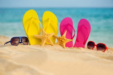 Sarı ve pembe sandalet gözlükle deniz arka planı kum stand