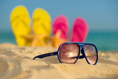 Sarı ve pembe sandalet gözlükle deniz arka planı kum stand