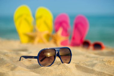 Sarı ve pembe sandalet gözlükle deniz arka planı kum stand
