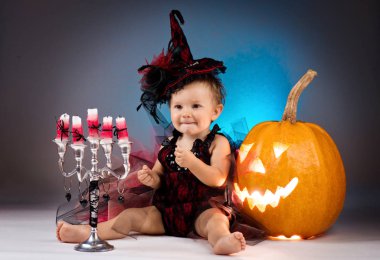 Küçük cadı kız çocuk gülüyor kabaklar ve mumlar arasında.