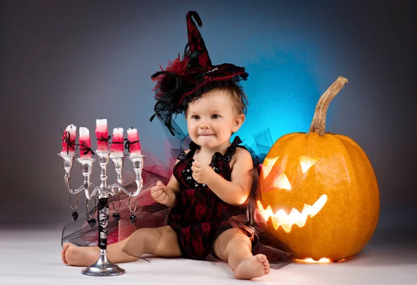 Küçük cadı kız çocuk gülüyor kabaklar ve mumlar arasında.