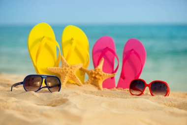 Sarı ve pembe sandalet gözlükle deniz arka planı kum stand