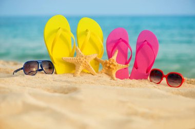 Sarı ve pembe sandalet gözlükle deniz arka planı kum stand