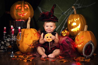 Küçük cadı kız çocuk gülüyor kabaklar ve mumlar arasında.