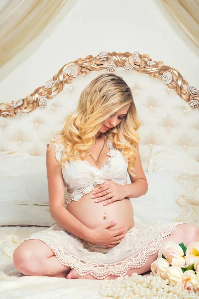 Красивая беременная брюнетка сидит на кровати в позе лотоса — стоковое фото