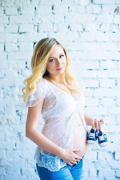 En vacker gravid flicka med sneakers för barn håller nära magen. — Stockfoto