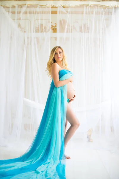 Beautiful pregnant woman. Attractive blonde touching naked belly posing in blowing drapery dress flying on wind — Stock Photo, Image