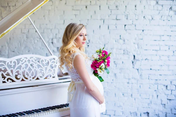 Schöne schwangere Frau mit einem Blumenstrauß im Inneren wartet auf das Baby. Schwangerschaft. — Stockfoto