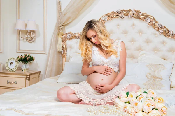 lotus pozisyonunda bir yatakta oturmuş güzel hamile esmer