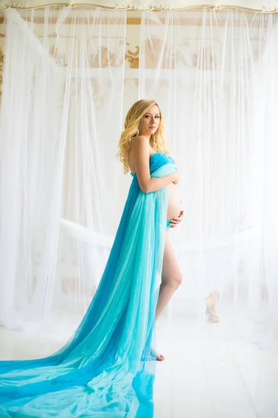 Beautiful pregnant woman. Attractive blonde touching naked belly posing in blowing drapery dress flying on wind — Stock Photo, Image