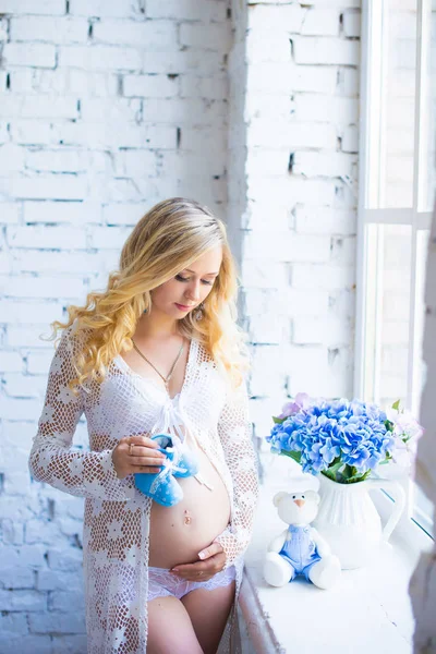 Çekici hamile kız çocuk ayakkabı ile cam kenarında duruyor.