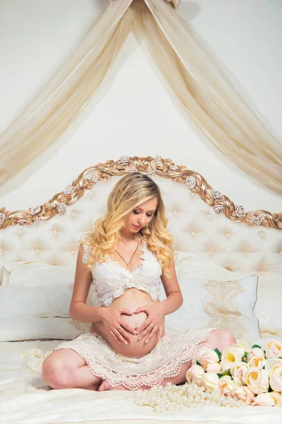 Schöne schwangere Brünette sitzt auf einem Bett in der Lotus-Position — Stockfoto