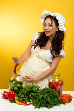 Neşeli bir hamile kadın bir koruma sebze sarı bir arka plan üzerinde yapar..