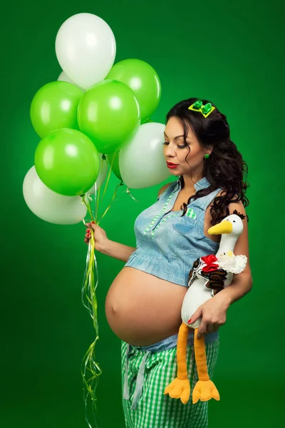 Femeie gravidă cu baloane și barză pe un fundal verde. Se uită la burtă, anticipând . — Fotografie, imagine de stoc