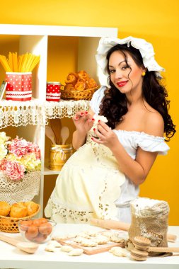 Güzel bir hamile kadın mutfakta beyaz bir elbise içinde büyük bir göbek ile bir yemek hazırlar.