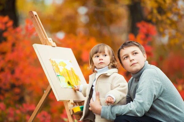 Um irmão e uma irmã felizes estão pintando em um parque de outono. Na natureza, caminhe ao ar livre — Fotografia de Stock
