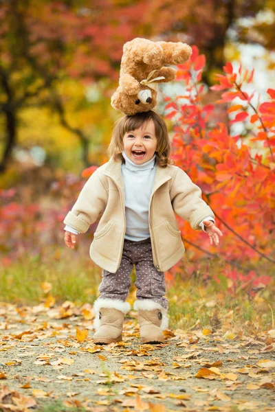 Meisje met een teddybeer in haar hand op een achtergrond van herfst gebladerte. Herfst tijd. — Stockfoto