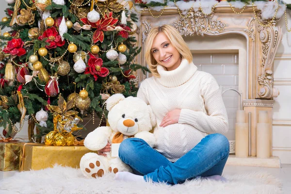Embarazo y Navidad, personas y concepto de expectativa - mujer embarazada feliz tocando su vientre en casa sobre un fondo de árbol de Navidad —  Fotos de Stock