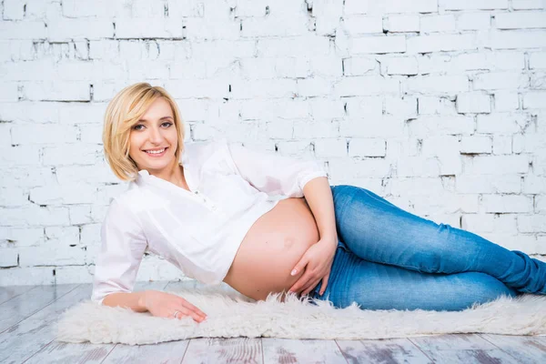 Mujer embarazada en jeans y camisa acostada. Esperando la felicidad . — Foto de Stock