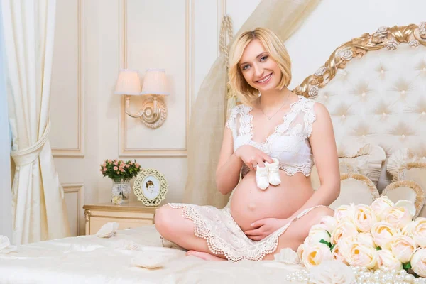Krásná těhotná blondýna sedí na posteli v lotosu představují — Stock fotografie