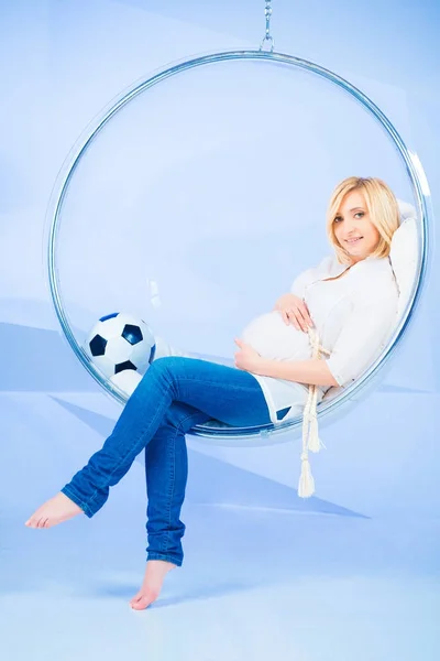 Mujer embarazada en una silla redonda con una pelota sobre un fondo azul — Foto de Stock