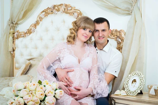 Krásný pár, těhotná mladá žena a muž objímá Láska Polibky, sedící na posteli v domácí interiér. — Stock fotografie