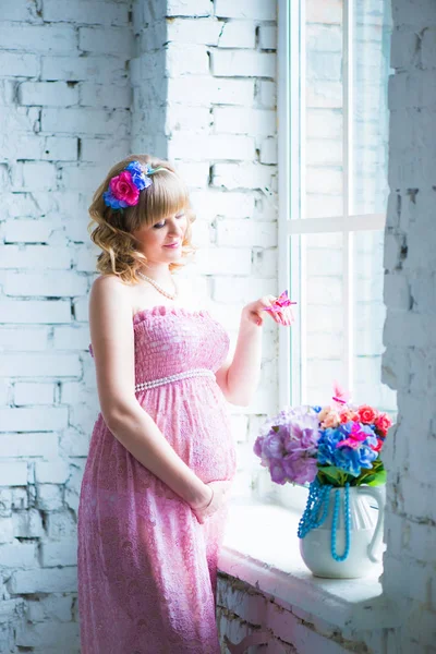 Gülümseyerek, göbek seyir, çiçek tutan hamile bir kadın. pembe elbise. — Stok fotoğraf