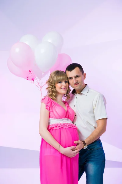Hermosa pareja joven esperando la felicidad, de pie en el estudio con globos sobre fondo rosa — Foto de Stock