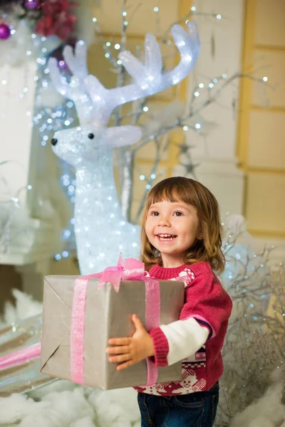 一个快乐的女孩站在她手中的礼物, 在一个新的年头鹿的背景. — 图库照片