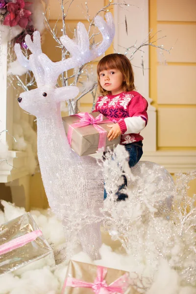 Une petite fille joyeuse avec un cadeau dans ses mains s'assoit sur un cerf . — Photo