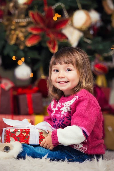 Glückliches Mädchen mit einem Geschenk in der Hand auf dem Hintergrund eines Neujahrsbaumes. — Stockfoto