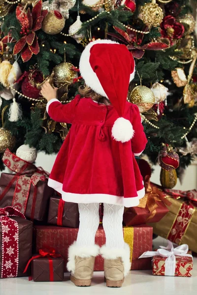 Vrolijk kerstfeest en Happy Holidays. Schattig klein kind meisje is het versieren van de kerstboom binnenshuis. — Stockfoto