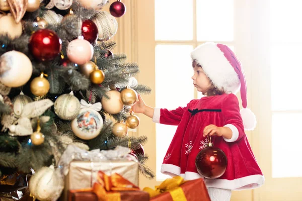 Feliz Navidad y Felices Fiestas. Linda niña está decorando el árbol de Navidad en el interior . —  Fotos de Stock