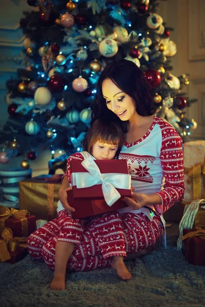Joven madre y sus dos hijas abriendo un mágico regalo de Navidad junto a un árbol de Navidad . —  Fotos de Stock